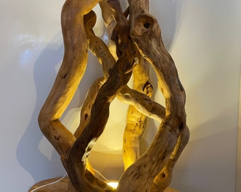 Puede incluir: Una lámpara de mesa de madera única con ramas de madera flotante entrelazadas. La lámpara emite un brillo cálido desde su fuente de luz interna. La base es una losa de madera natural, lo que se suma a la estética orgánica. Una pieza decorativa.