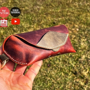 May include: A brown leather glasses case with a flap closure and a light brown leather accent. The case has white stitching and a metal ring.