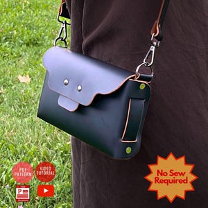 Peut inclure: Sac bandoulière en cuir noir et gris avec rabat festonné et accessoires argentés. Le sac a un rabat gris clair contrastant avec deux rivets argentés. La bandoulière est noire et marron avec un motif coloré. L'étiquette indique "No Sew Required".