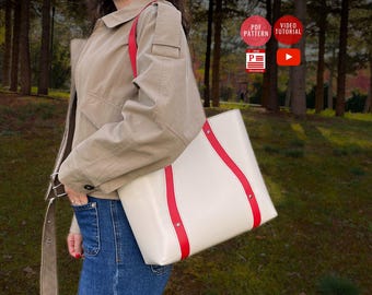 May include: A white tote bag with red trim and silver hardware. The bag has a long strap and is being held by a person wearing a beige jacket and blue jeans.