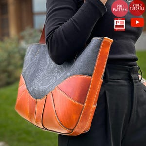 May include: A leather tote bag with a grey paisley design, orange and brown leather panels, and a long shoulder strap. The bag has visible stitching. The image also includes text that says "PDF PATTERN" and "VIDEO TUTORIAL".