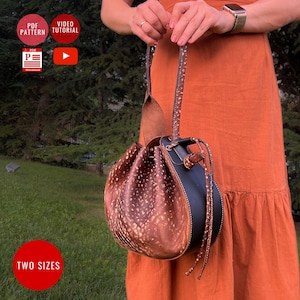 May include: A handcrafted leather bag with a unique spotted pattern and a dark blue accent. The bag features a drawstring closure and a long strap. The image also shows the text "TWO SIZES".