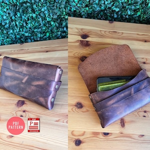 Könnte beinhalten: Eine braune Leder-Handyhülle mit einer Klappe, die mit einem Druckknopf geschlossen wird. Die Hülle ist geöffnet und ein grünes Handy befindet sich im Inneren. Die Hülle liegt auf einer Holzoberfläche.