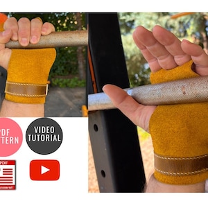 May include: A pair of yellow leather weightlifting grips with brown leather wrist straps. The grips are shown being worn on a person's hands while holding a barbell.