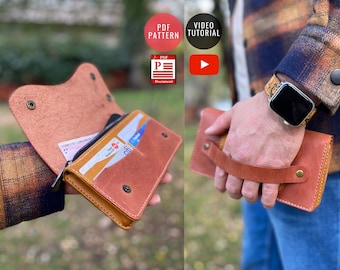 May include: A brown leather wallet with a zipper closure and a handle. The wallet is open to show the interior, which has a zippered pocket, card slots, and a bill compartment. The wallet is being held by a person's hand.