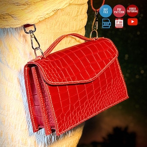 Puede incluir: Un bolso de mano rojo brillante con un patrón texturizado de piel de cocodrilo, que cuenta con un asa superior, una solapa plegable y clips de metal para una correa. La imagen incluye iconos de DXF FILE, PDF PATTERN y VIDEO TUTORIAL arriba.