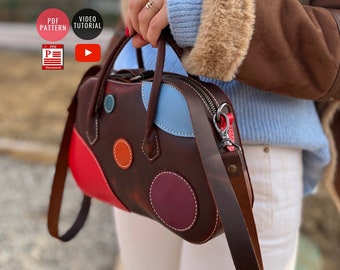 May include: A brown leather handbag with a colorful patchwork design. The bag has a top handle and a long shoulder strap. The strap has a red metal clasp. The bag is decorated with colorful circles.
