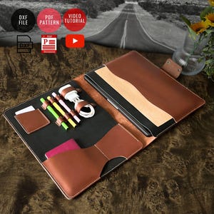 Może przedstawiać: Brązowe skórzane portfolio z czarnym wnętrzem, mieszczące tablet. Posiada jasny wzór w paski i wiele kieszeni. Akcesoria obejmują długopisy, kabel ładujący i mały uchwyt na karty. Portfolio jest otwarte, prezentując zawartość.