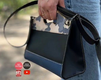 May include: A blue, black, and white leather handbag with a camouflage pattern on the top flap. The bag has a top handle and a long shoulder strap.