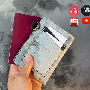 May include: A gray leather passport holder with a yellow stitch detail and a pocket for cards. The holder is open and a passport is visible inside. The image includes the text "PDF PATTERN" and "VIDEO TUTORIAL".