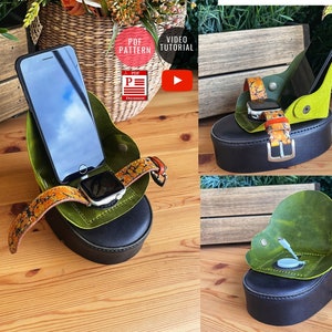 May include: A green leather phone and watch stand with a black base. The stand has a slot for a phone and a watch band. The watch band is orange and black with a floral pattern. The stand is on a wooden surface. "PDF Pattern" and "Video Tutorial" are written on the image.