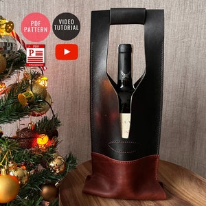 Może przedstawiać: Czarny skórzany pojemnik na butelkę wina z czerwonym skórzanym dnem. Pojemnik ma uchwyt i wycięcie na butelkę. Butelka jest widoczna przez wycięcie.