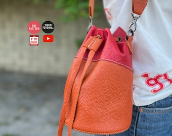 Puede incluir: Un bolso de cubo de cuero naranja y rojo de dos tonos con cierre de cordón y una correa de cadena plateada. El bolso lo lleva una persona. La imagen también incluye texto que dice "PDF Pattern" y "Video Tutorial".