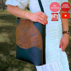 Può includere: Borsa a tracolla in pelle verde scuro con un inserto in pelle marrone fantasia. La borsa ha una lunga tracolla ed è tenuta da una persona. La borsa ha un design unico ed è probabilmente fatta a mano. La borsa è un accessorio elegante.