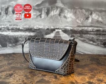 May include: A small, brown leather crossbody bag with a black leather flap and a crocodile-embossed pattern. The bag has a silver chain strap and a silver buckle closure.