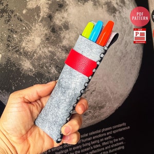 May include: A gray felt pencil case with a red zipper pull and black stitching. Three colorful markers are inside the case.