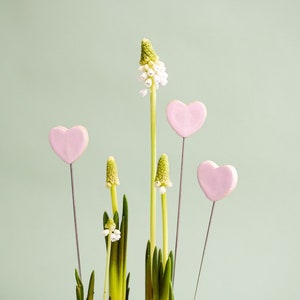 Könnte beinhalten: Ein Strauß weißer Blumen mit rosafarbenen herzförmigen Keramikdekorationen an Stielen.
