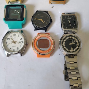Puede incluir: Una colección de ocho relojes de pulsera y cabezales de reloj Casio con diversos diseños, incluyendo modelos de calculadora digital, esferas analógicas blancas o negras y cajas de plástico de colores amarillo, turquesa y naranja, con una correa de eslabones metálicos.