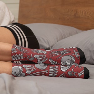 May include: A pair of red ankle socks with a white anatomical skeletal design. The socks feature bones, skulls, and other anatomical details.