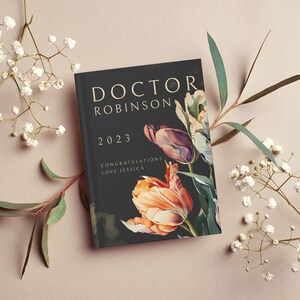 Pu&ograve; includere: Un biglietto nero con lettere dorate che recitano "Doctor Robinson 2023 Congratulazioni Love Jessica" con un disegno floreale con tulipani colorati.