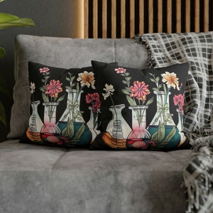 May include: Two black throw pillows with a floral design featuring colorful flowers in glass beakers. The pillows are on a gray couch.