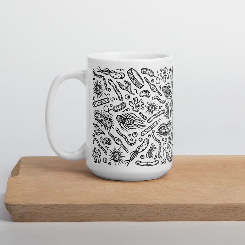 May include: White ceramic mug with a black and white illustration of various bacteria and microbes. The mug is on a wooden surface.