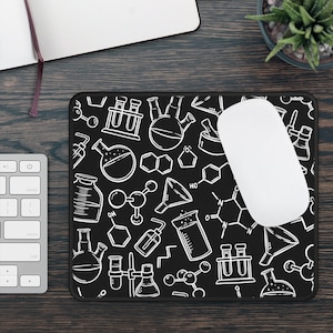 May include: Black mouse mat with a white pattern of science-related illustrations, including beakers, flasks, and molecules. The mouse mat is on a dark wood surface.