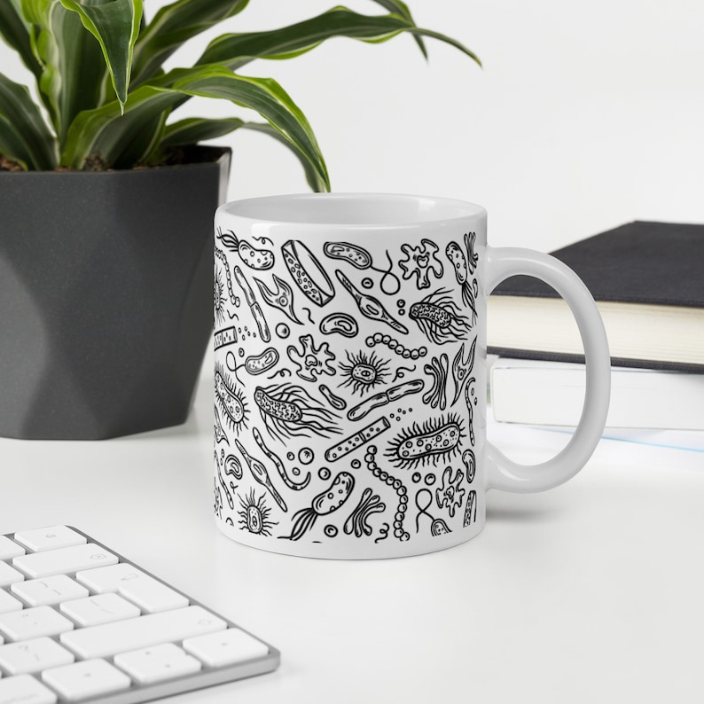 May include: White ceramic mug with a black and white illustration of various bacteria and microbes. The mug has a handle on the right side.