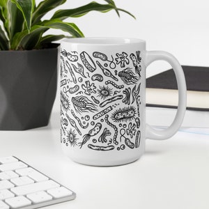 May include: White ceramic mug with a black and white illustration of various bacteria and microbes. The mug has a handle on the right side.
