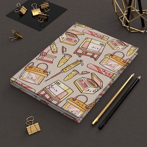 Pode incluir: Um caderno bege com um padrão colorido de equipamentos de laboratório científico, incluindo béqueres, tubos de ensaio, pipetas e réguas. O equipamento é desenhado em estilo de desenho animado com rostos fofinhos.