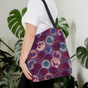 May include: A purple tote bag featuring a pattern of red, pink, and blue cells. The bag has black straps and is made from a durable fabric.