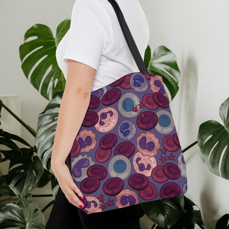 May include: A purple tote bag featuring a pattern of red, pink, and blue cells. The bag has black straps and is made from a durable fabric.