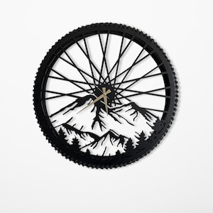 May include: Black metal wall clock with a mountain silhouette design cut out of a bicycle wheel rim. The clock hands are gold.