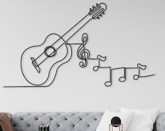Op de afbeelding: Een zwarte metalen wandsculptuur van een gitaar en muzieknoten. De sculptuur is gemonteerd op een witte muur boven een grijze bank met een bruine deken. De bank staat in een woonkamer met een salontafel en decoratieve items.