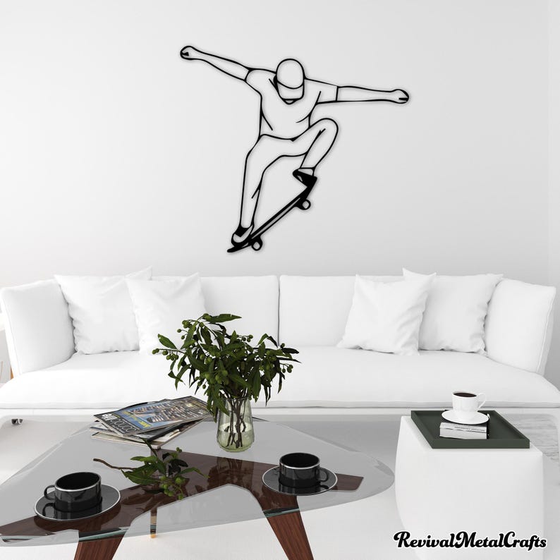 May include: Black metal wall art of a person skateboarding. The art is mounted on a white wall above a white couch with a glass coffee table and a small potted plant.