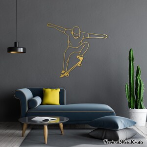 May include: Gold metal wall art depicting a person skateboarding. The art is mounted on a gray wall with a blue couch and a cactus plant in the background.