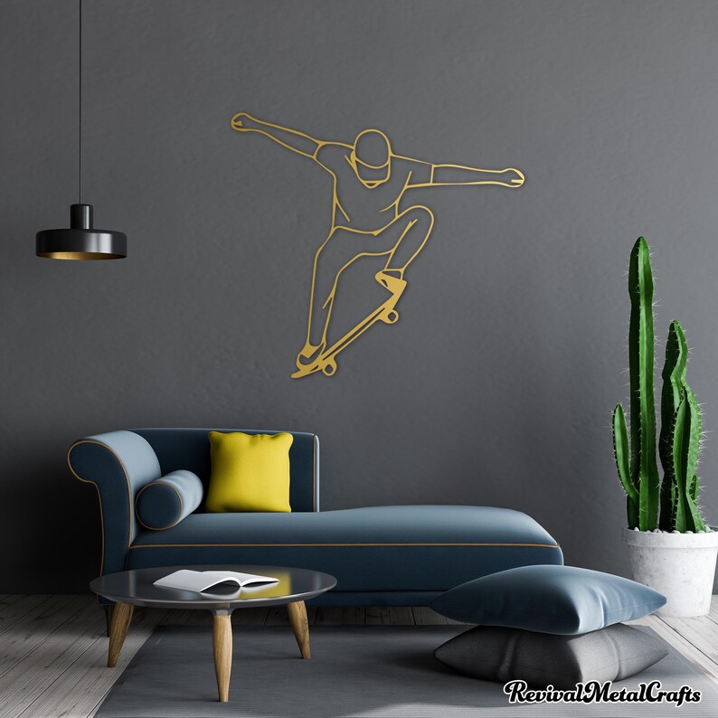 May include: Gold metal wall art depicting a person skateboarding. The art is mounted on a gray wall with a blue couch and a cactus plant in the background.
