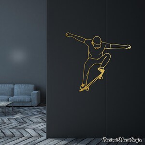 May include: Gold silhouette wall decal of a person skateboarding. The person is wearing a hat and is in mid-air with their board.
