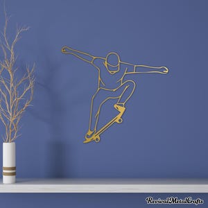 May include: Gold metal wall art of a person skateboarding. The person is outlined in gold metal and is in mid-air, with one leg extended and the other bent. The skateboard is also outlined in gold metal and has wheels.