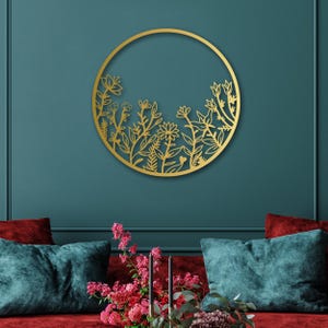 May include: Gold metal wall decor featuring a circular design with a floral pattern. The design is reminiscent of a garden with various flowers and leaves.