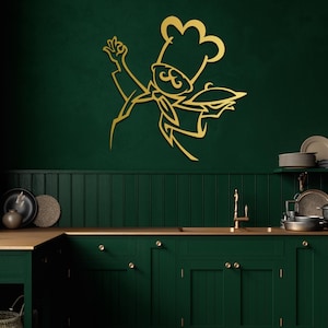 May include: A gold-colored metal wall art piece featuring a stylized line drawing of a chef wearing a tall hat and a neckerchief, holding a serving platter with one hand raised in a gesture, mounted on a dark green kitchen wall surface.