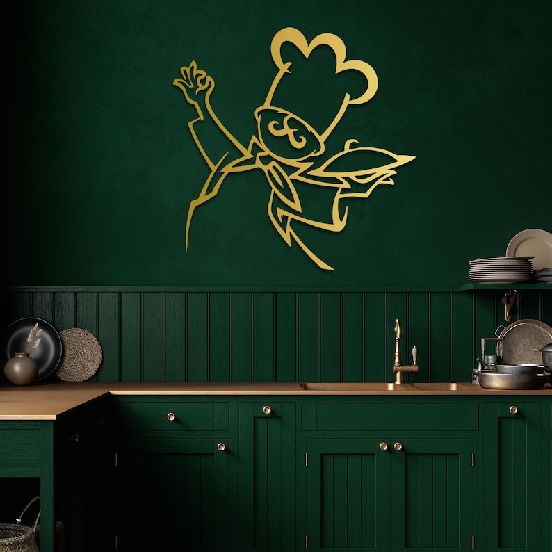 May include: A gold-colored metal wall art piece featuring a stylized line drawing of a chef wearing a tall hat and a neckerchief, holding a serving platter with one hand raised in a gesture, mounted on a dark green kitchen wall surface.