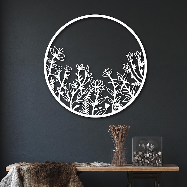 May include: White metal wall decor featuring a circular frame with a floral design. The design includes various flowers, leaves, and stems.