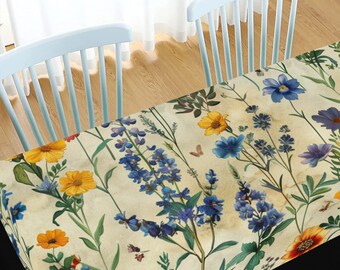 May include: A rectangular tablecloth with a floral pattern featuring blue and yellow flowers on a cream background. The tablecloth is made of a soft, durable fabric and is perfect for adding a touch of elegance to any dining table.