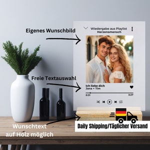 May include: A wooden photo frame with a digital music player and a picture of a couple. The frame has a white background and a black border. The music player has a black background and white buttons. The picture shows a couple smiling at the camera. The text "Ich liebe dich Jana + Tim" is displayed on the music player.
