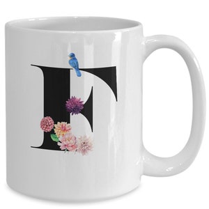 May include: White ceramic mug with a black letter "F" decorated with watercolor flowers and a blue bird.