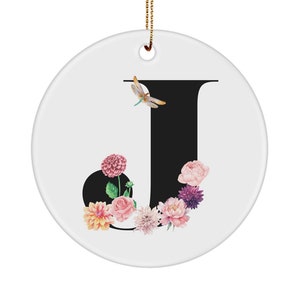 May include: A white ceramic ornament with a black letter J surrounded by pink, purple, and yellow flowers and a dragonfly.