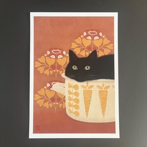 May include: A black cat sits inside a white ceramic pot with a yellow and orange floral pattern. The pot has two carrot designs on the front. The background is a red-orange color with a yellow and orange floral pattern.