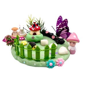 May include: A miniature fairy garden scene with a green play dough base, a red and white mushroom house, a white rabbit figurine, a purple butterfly, a pink mushroom figurine, and a green picket fence.