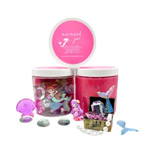May include: Two pink slime jars with mermaid themed decorations. One jar has a mermaid figurine, seashells, and gems. The other jar has a mermaid tail, a treasure chest, and pearls. The label on the jar reads "mermaid jar" and includes the text "non-toxic dough, gluten free, low consumption, made with flour, and essential oil. Small parts, ages 3+".